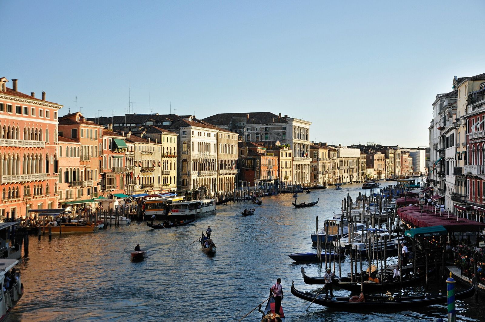 The Grand Canal seen from the Rialto Bridge, lined with palaces, gondolas and mooring poles in late-afternoon light